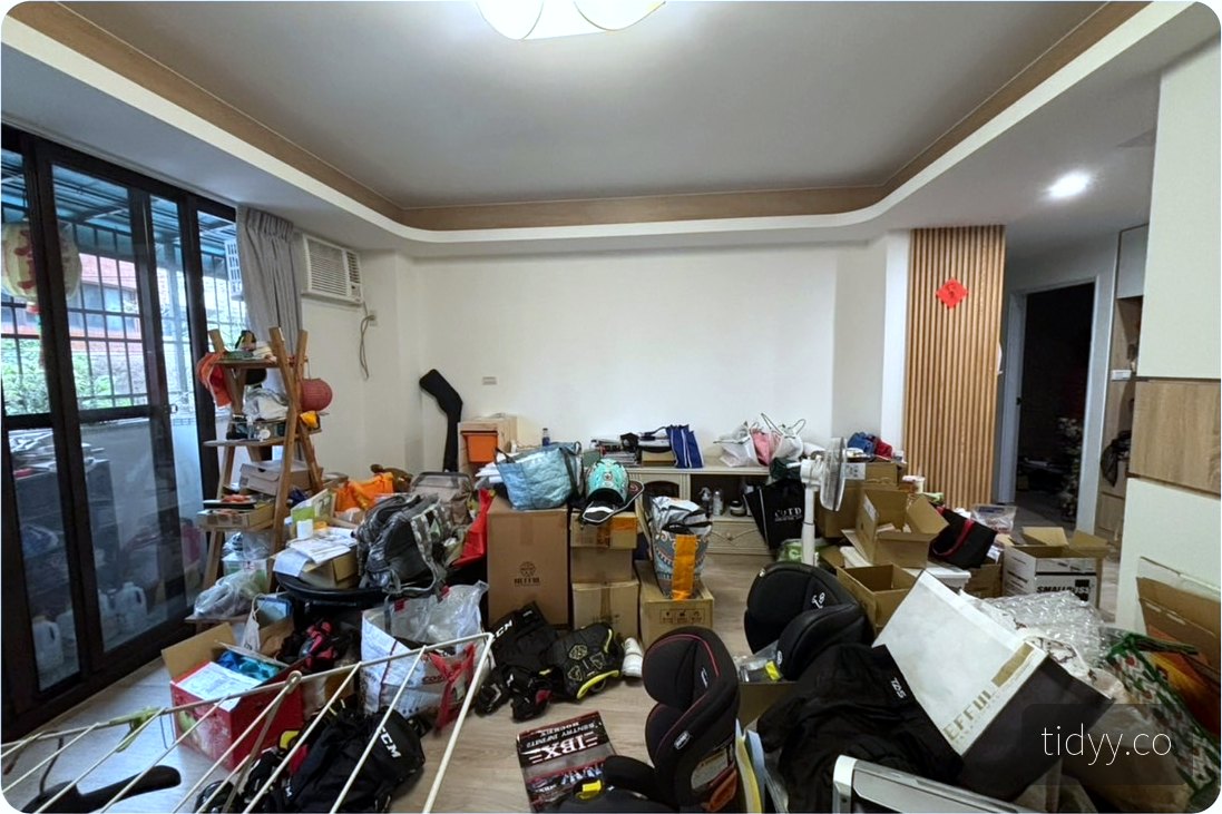 整理前的客廳，地面與走道堆滿紙箱、行李與雜物